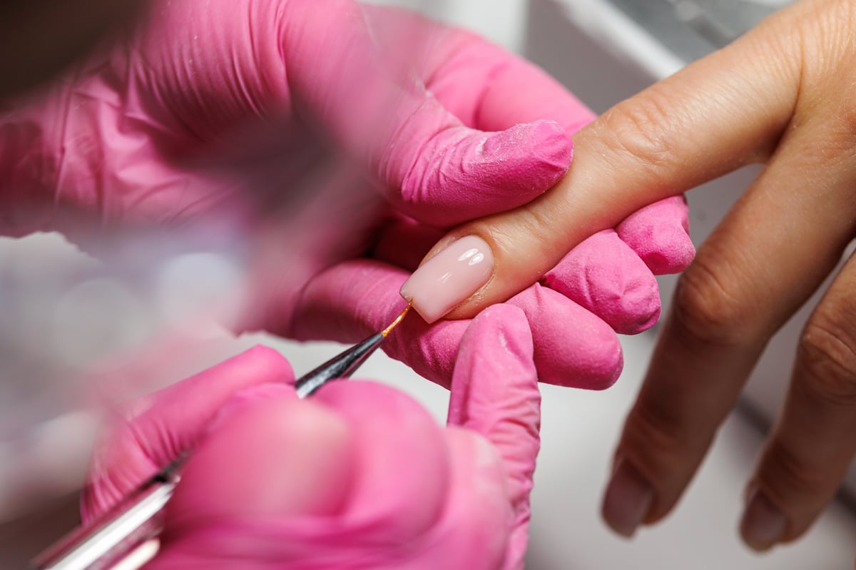 Close-up view of a beauty professional wearing pink gloves pushing back cuticles on a client's hand during manicure procedure, french nails.