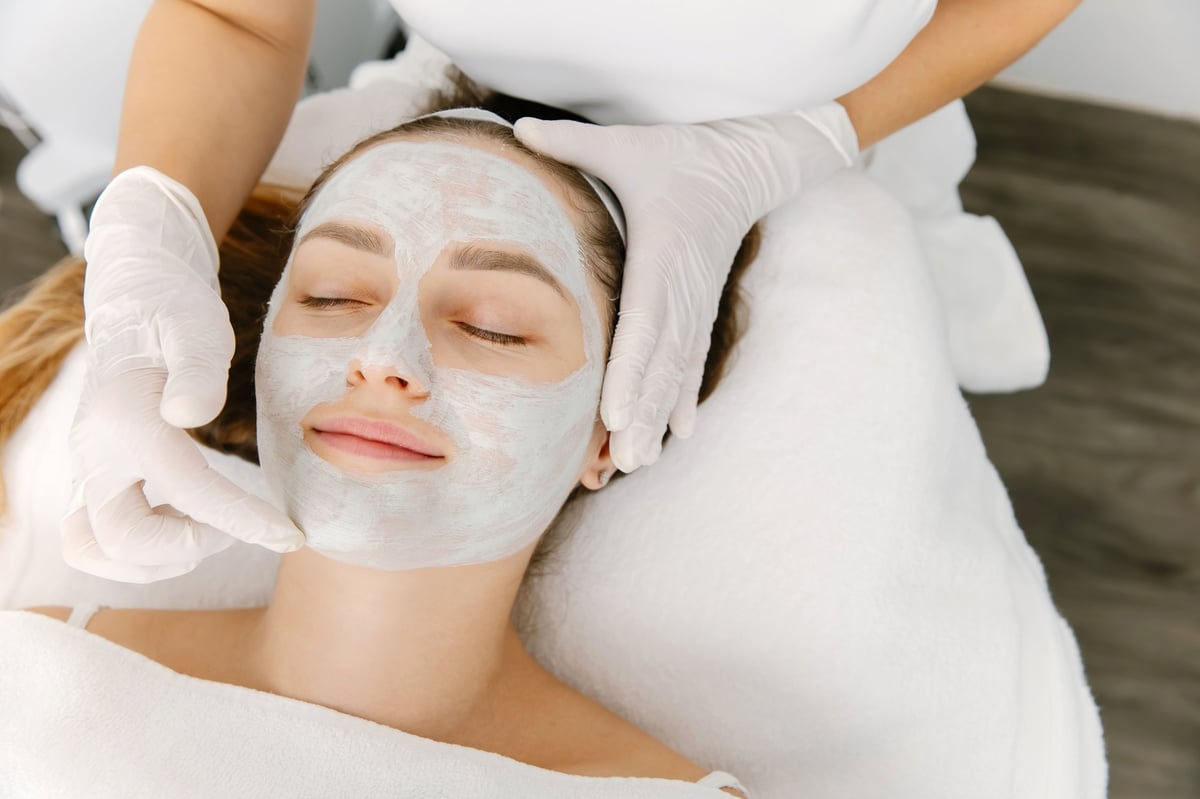 Woman receiving facial skincare treatment with natural ingredients mask applied by professional
