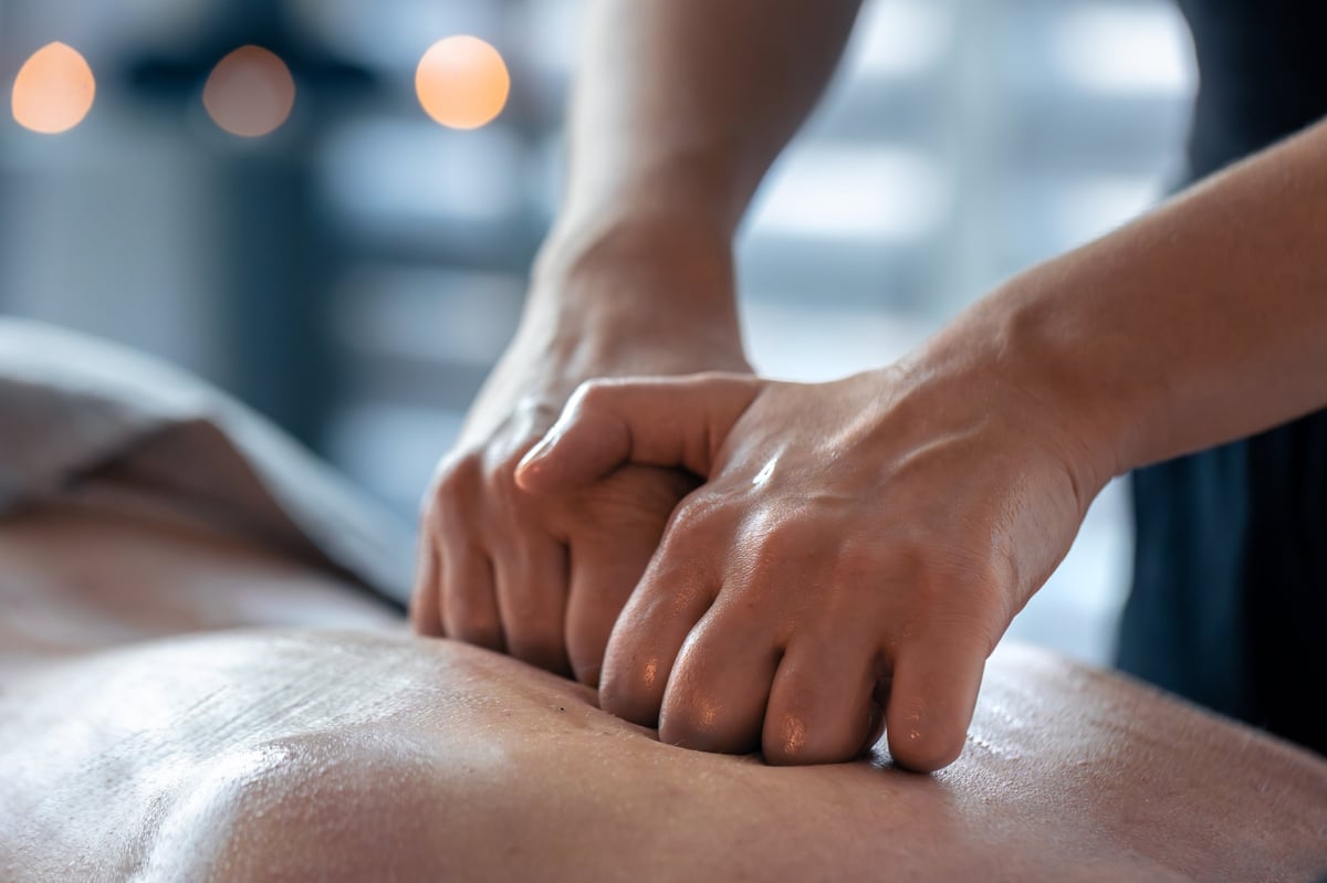 Two clenched hands press evenly on an oiled back. Texture and technique show a modern routine for daily balance and recovery
