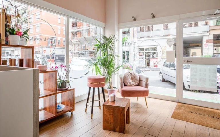 Bright modern storefront interior with potted plants, wooden furniture, and large windows overlooking a street