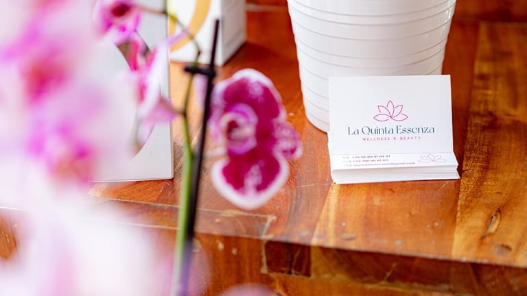 Business card for La Orquidea Esencias displayed on wooden surface with pink orchid flowers and white cup in background